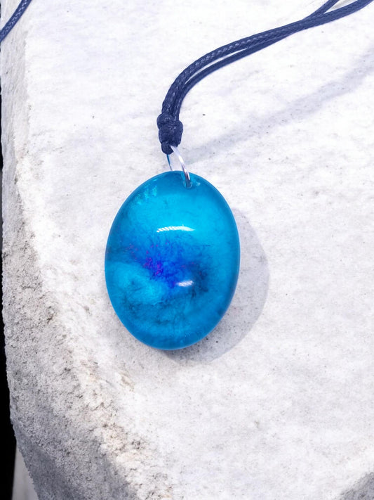 Artymunk3y blue resin oval pendant necklace with swirls of magenta and indigo on a black cord.