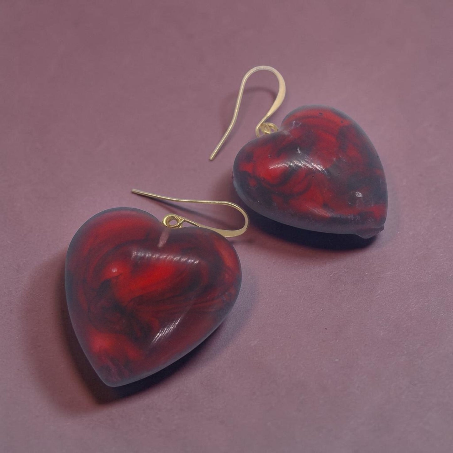 Artymunk3y heart shaped dangle earrings in marbled red and black resin with gold-tone hooks on a purple background.