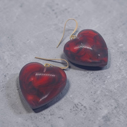 Artymunk3y heart-shaped dangle earrings in marbled red and black resin with gold-tone hooks on a grey surface.
