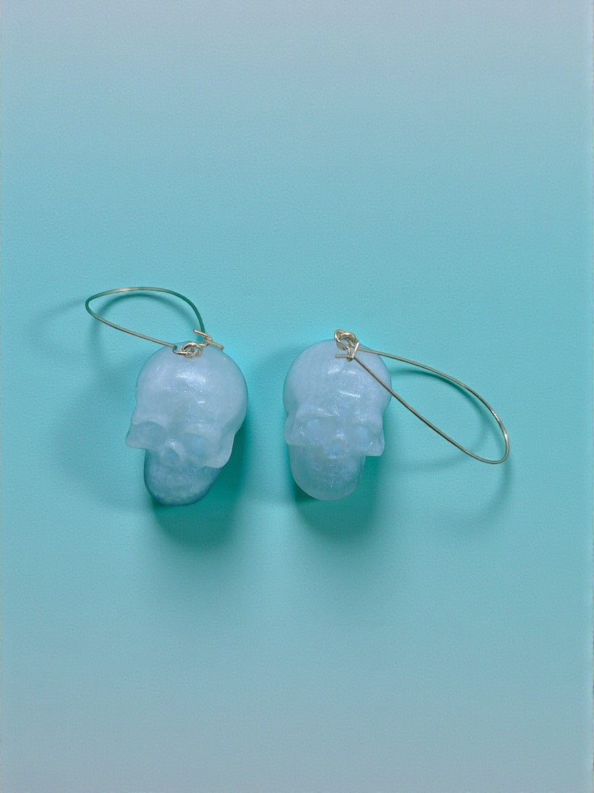 Artymunk3y pale blue translucent skull shaped dangling earrings with gold hoops.
