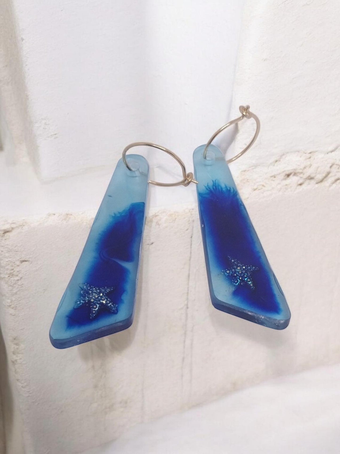 Artymunk3y blue resin drop earrings with glitter starfish charms and gold hoops. Translucent sky blue fades into deep ocean blue.