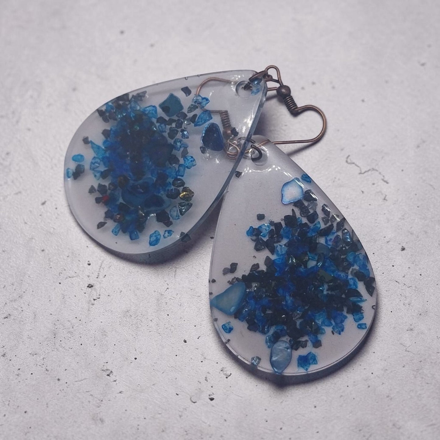 Artymunk3y teardrop dangle earrings featuring clear resin with deep blue crushed stone accents and rustic metal hooks.