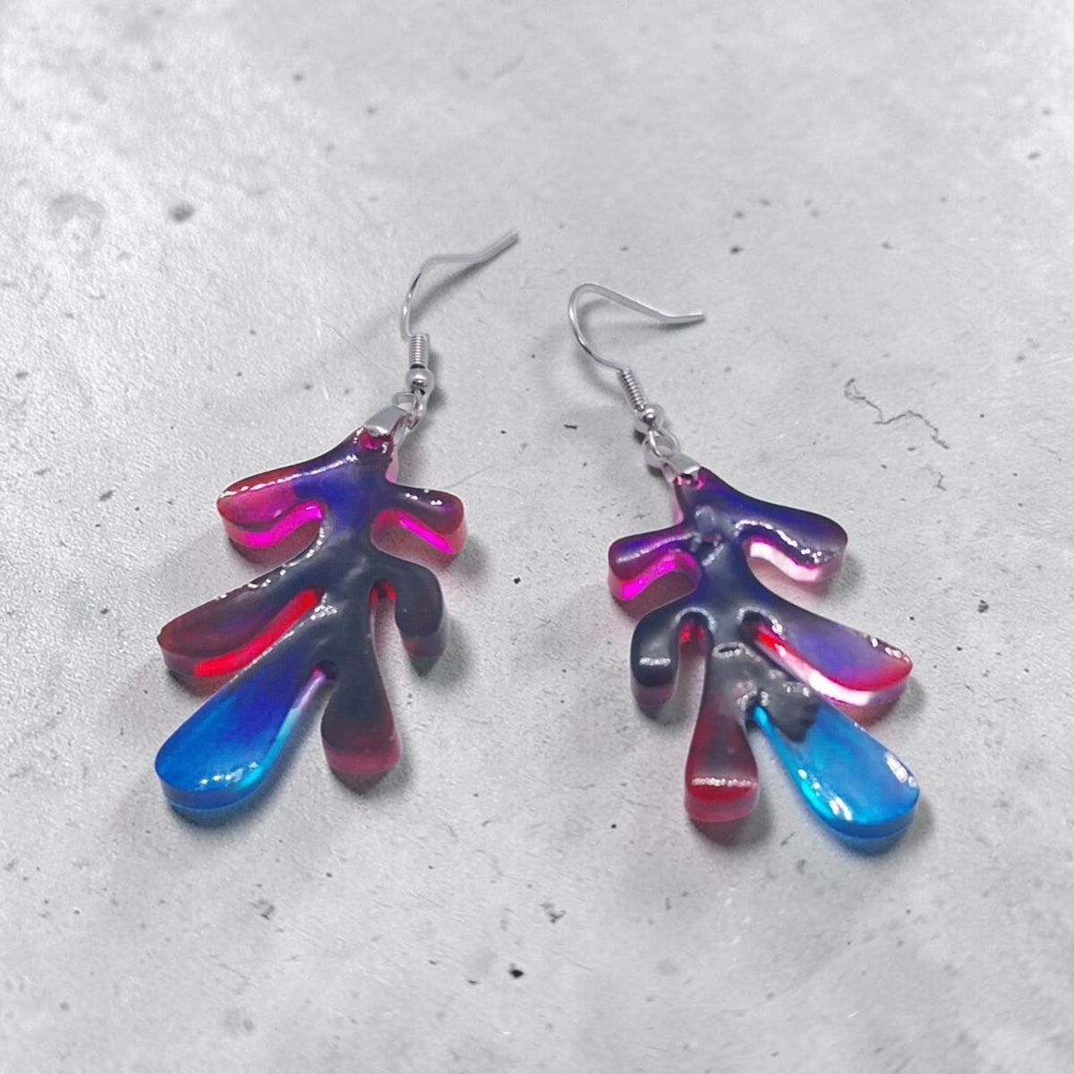 Artymunk3y abstract organic leaf-shaped resin drop earrings in a vibrant red, blue, and violet gradient on grey stone.