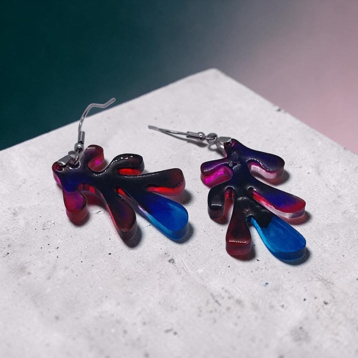 Artymunk3y abstract resin drop earrings with organic leaf shapes in a red, blue, and violet gradient on a stone base.