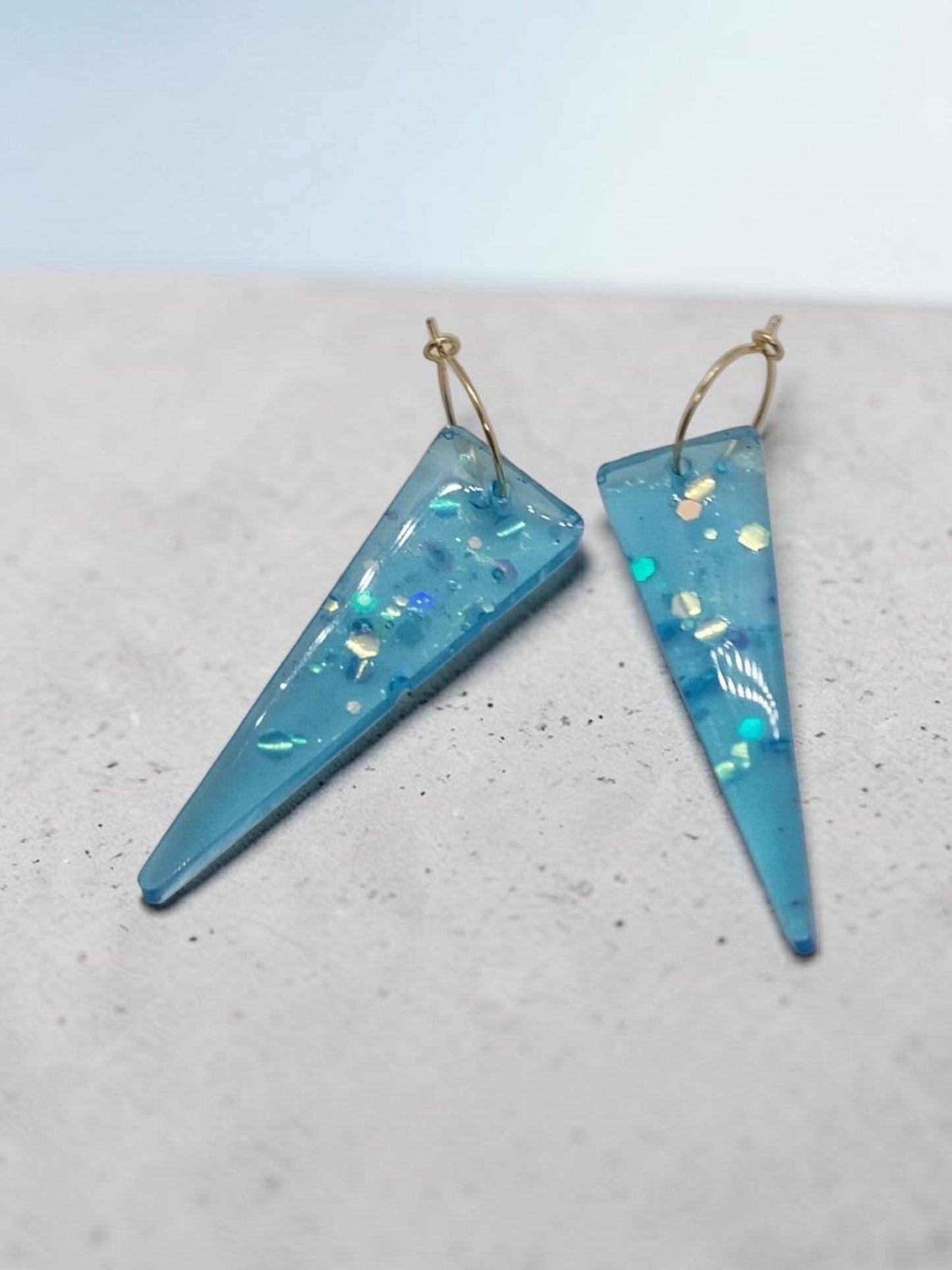 Artymunk3y blue resin drop earrings with glitter inclusions and gold-tone hoops. Elongated triangular shape.