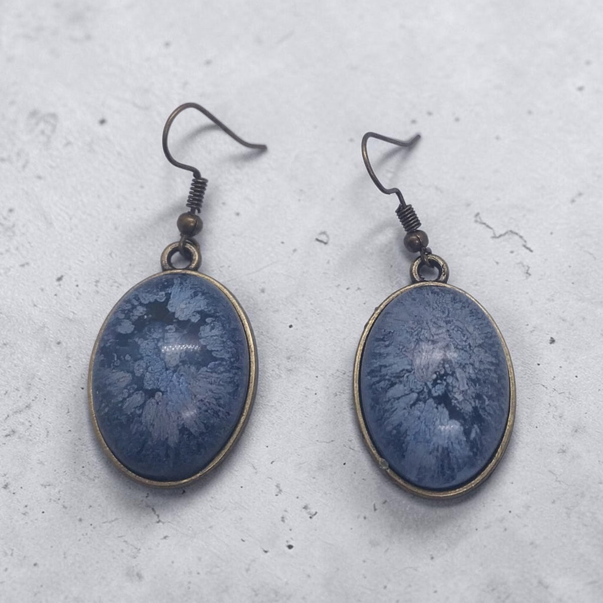 Artymunk3y oval drop earrings featuring blue resin inlay with frost-like patterns in antique bronze metal frames.