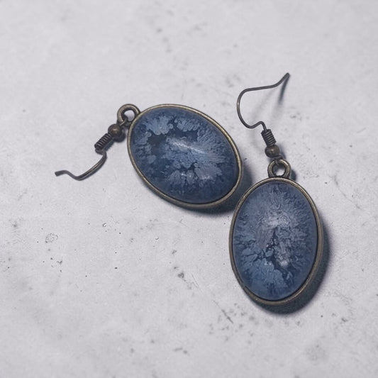 Artymunk3y oval drop earrings featuring blue resin inlay with frost-like patterns set in antique-bronze metal frames.