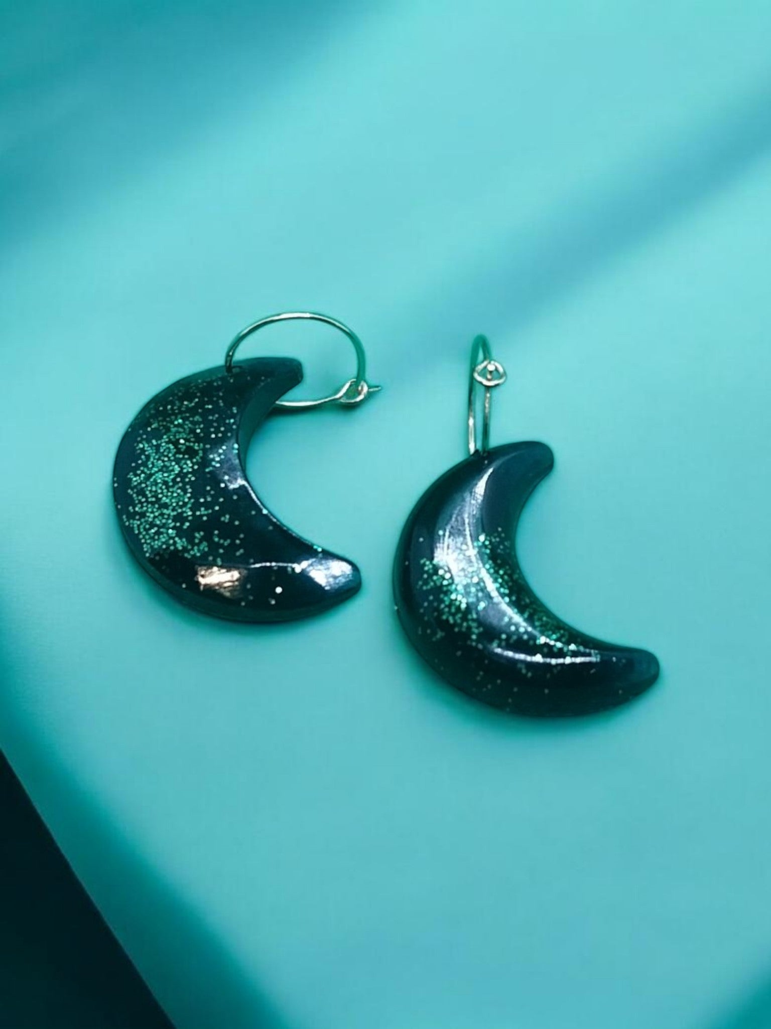 Artymunk3y dark crescent moon dangle earrings with green glitter accents.