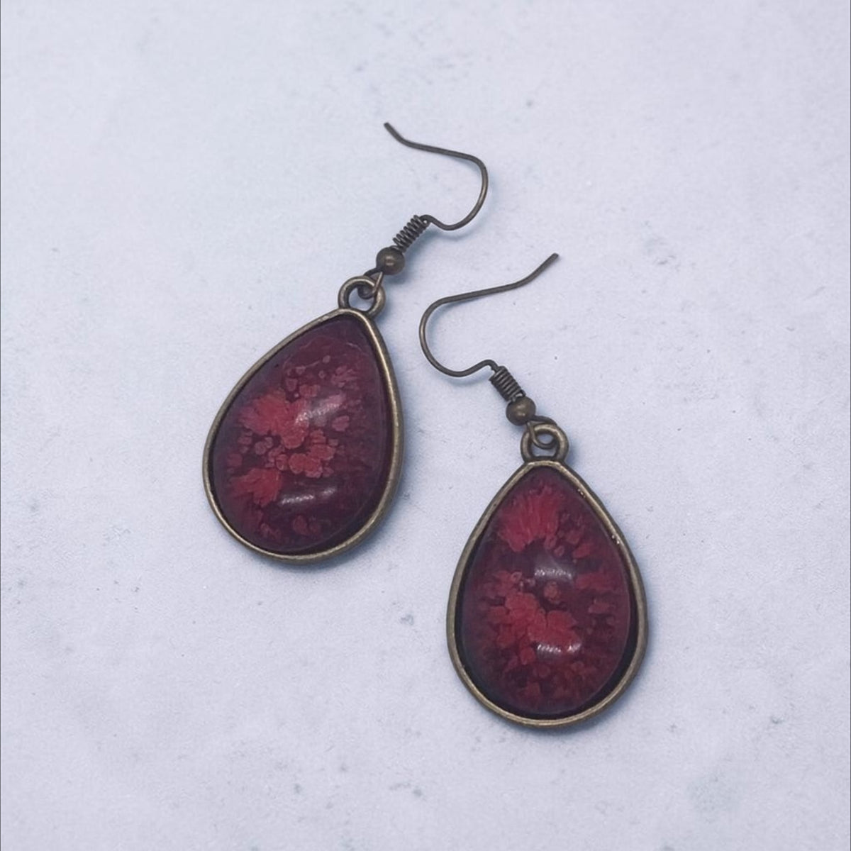 Artymunk3y teardrop dangle earrings featuring deep crimson resin with floral patterns in antique-bronze settings.