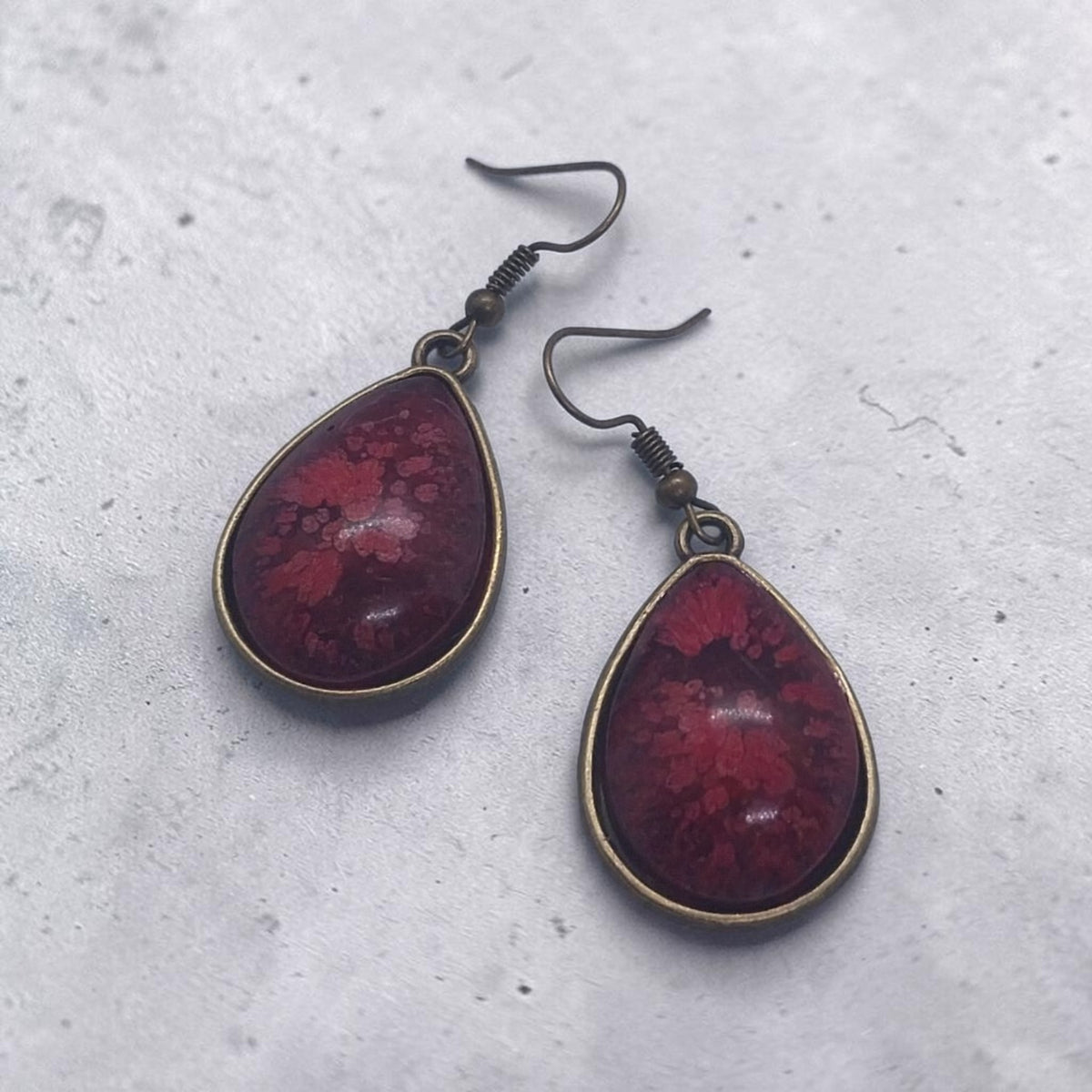 Artymunk3y teardrop dangle earrings featuring deep crimson resin with floral patterns in antique-bronze settings.