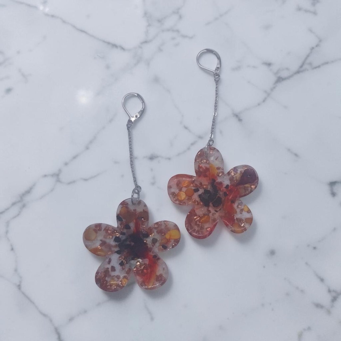 Artymunk3y floral drop earrings featuring clear resin flower pendants with amber, orange, and red confetti accents.