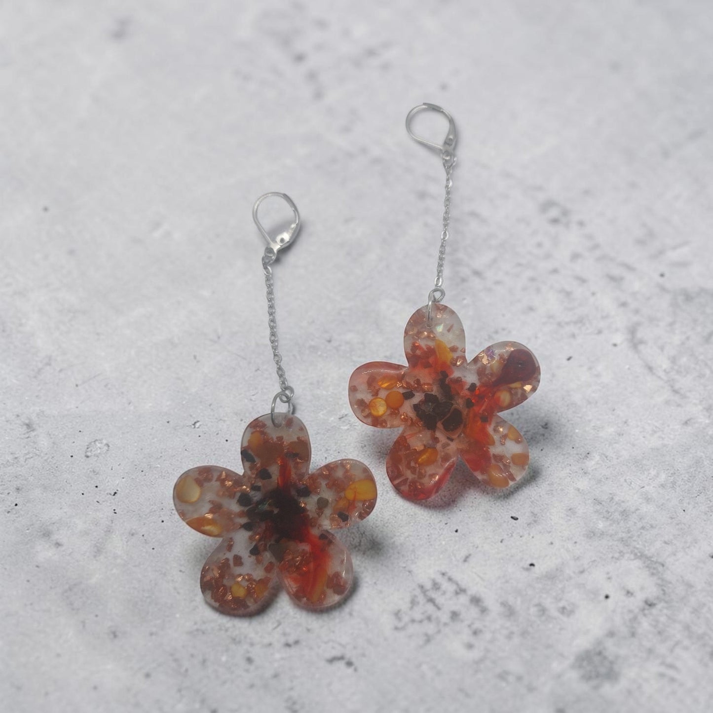Artymunk3y floral drop earrings featuring clear resin flower pendants with amber, orange, and red confetti accents.