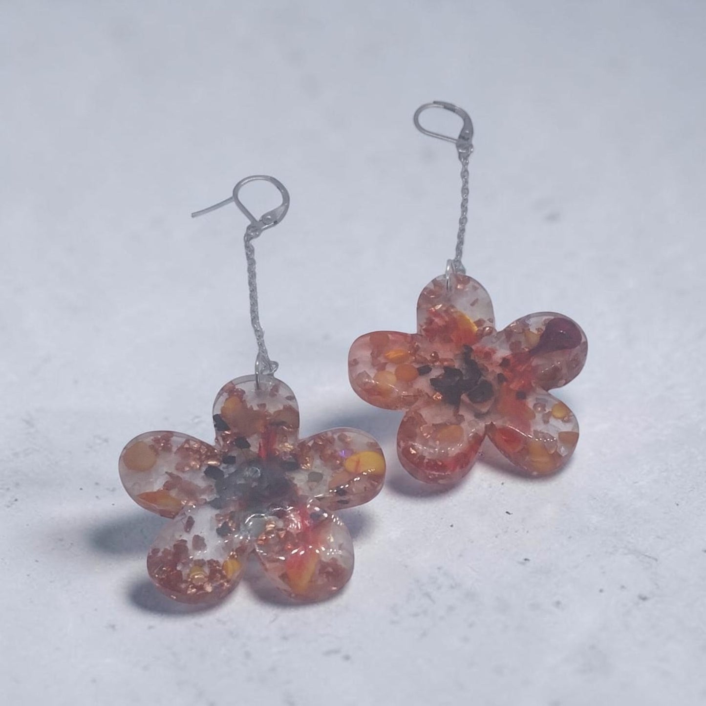 Artymunk3y floral drop earrings featuring clear resin flower pendants with amber, orange, and red confetti accents.