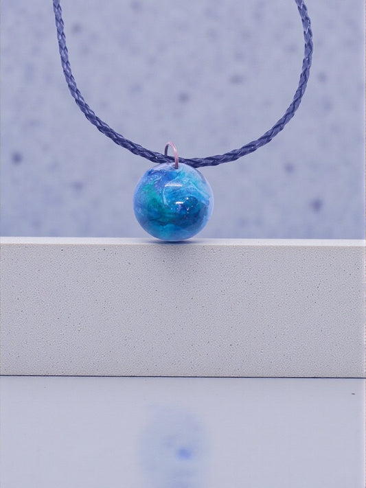Artymunk3y swirling galaxy orb pendant necklace in blue and green hues on a black braided cord.