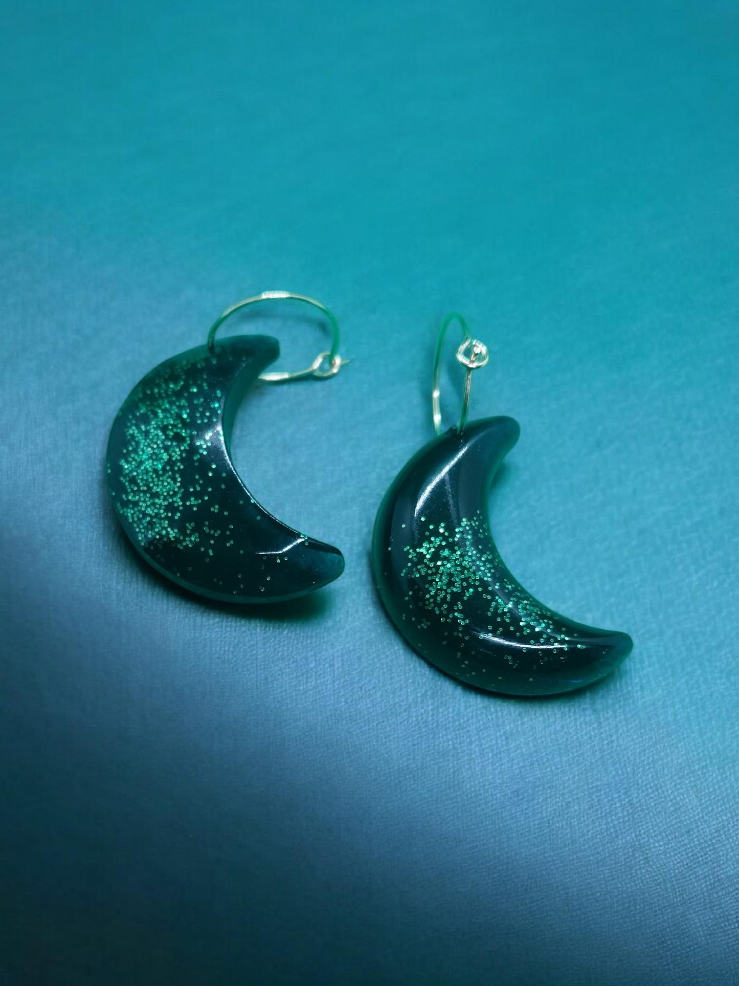 Artymunk3y dark green crescent moon dangle earrings with shimmering green glitter accents.