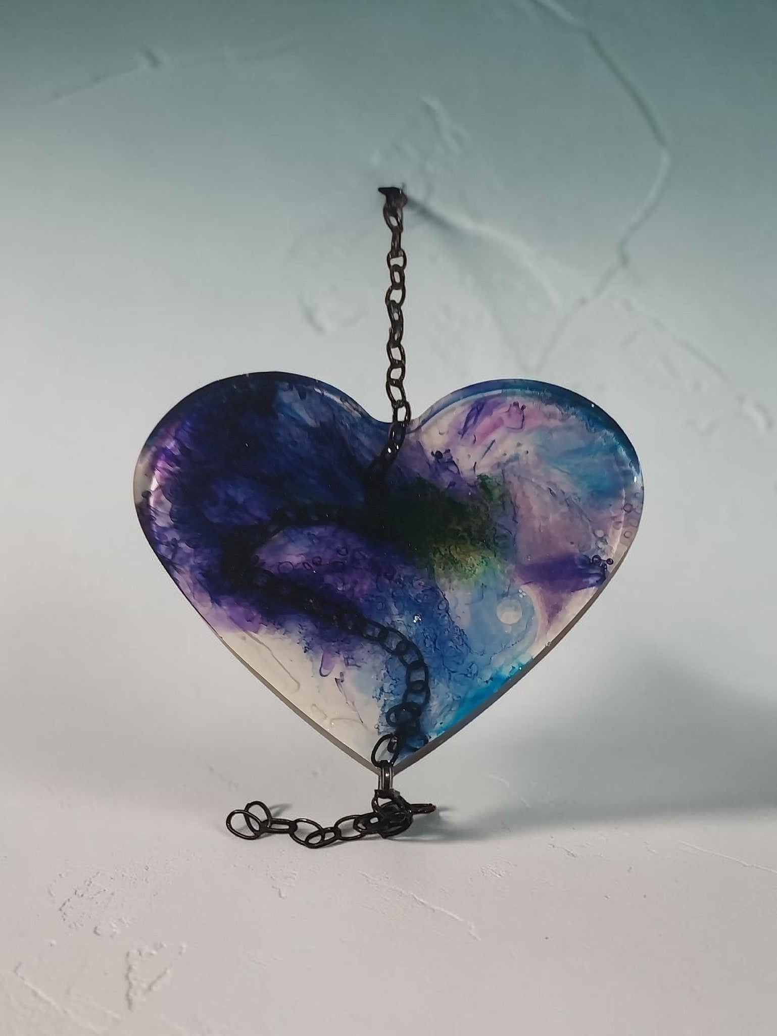 Artymunk3y hanging heart resin wall art decoration with swirling purple, blue, and green abstract patterns and a metal chain.