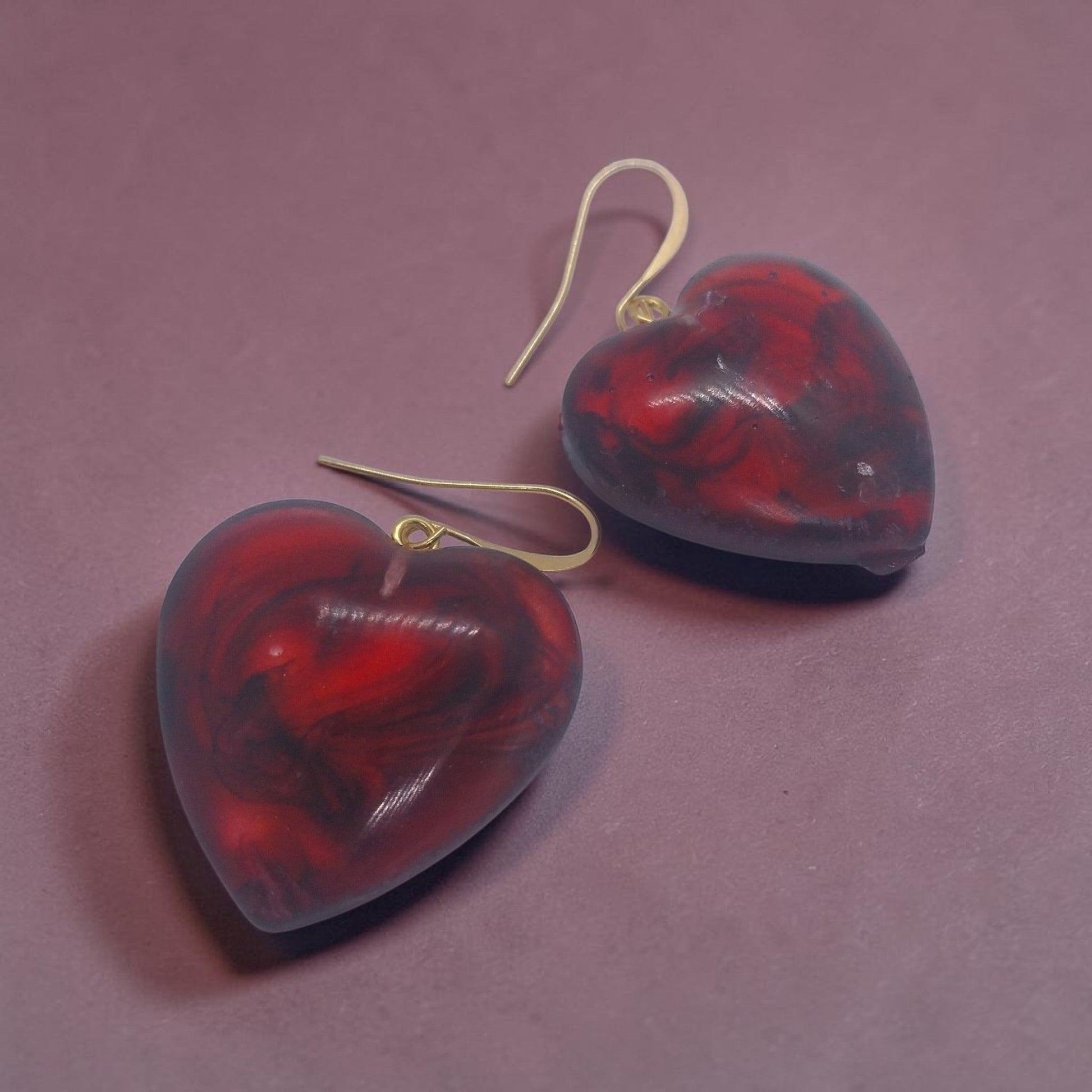 Artymunk3y heart shaped dangle earrings in marbled red and black resin with gold-tone hooks on a purple background.