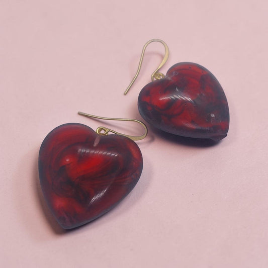 Artymunk3y heart-shaped dangle earrings in marbled red and black resin with gold-tone hooks on a pink background.