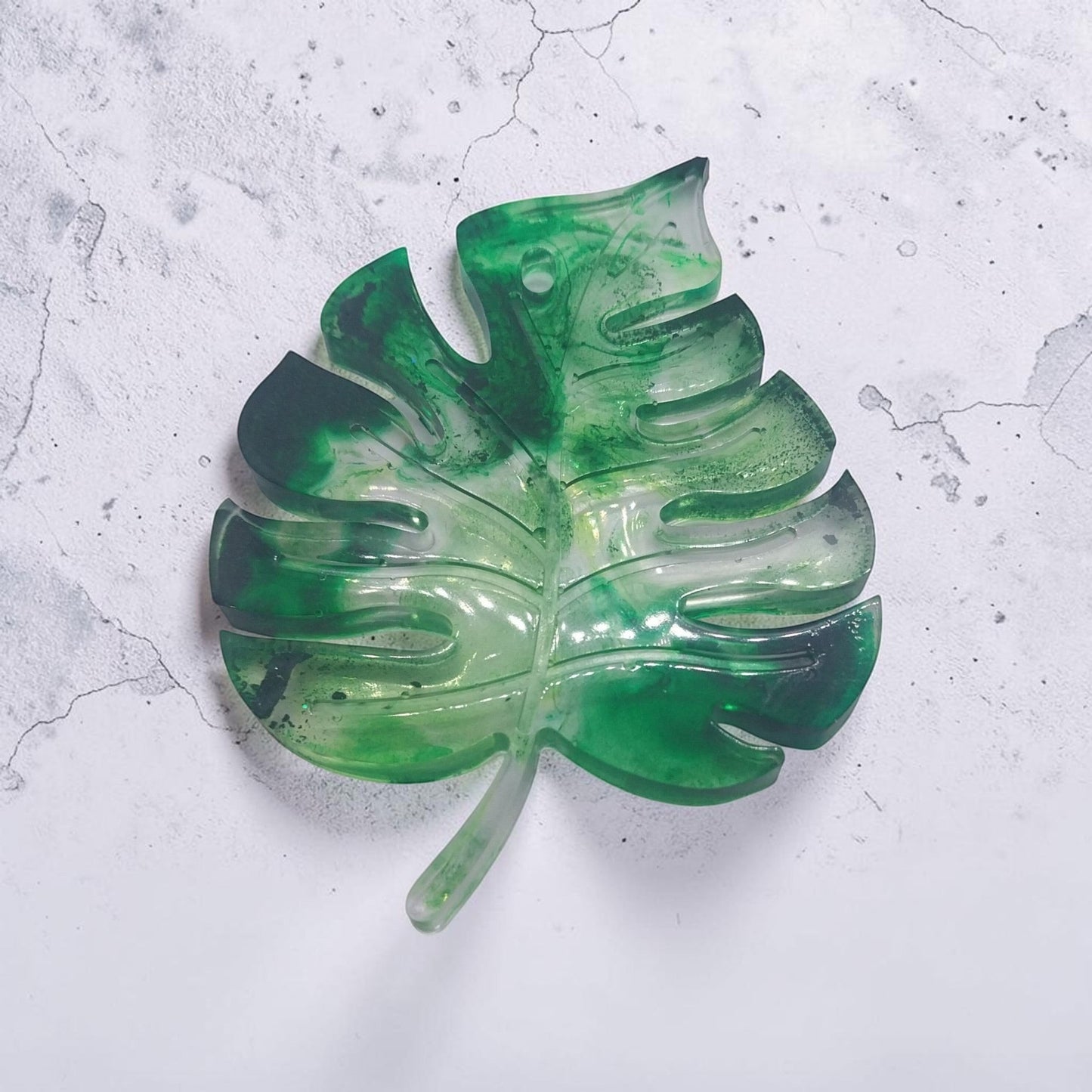 Artymunk3y monstera leaf shaped resin tray in marbled forest green with a glossy finish on a textured white surface.