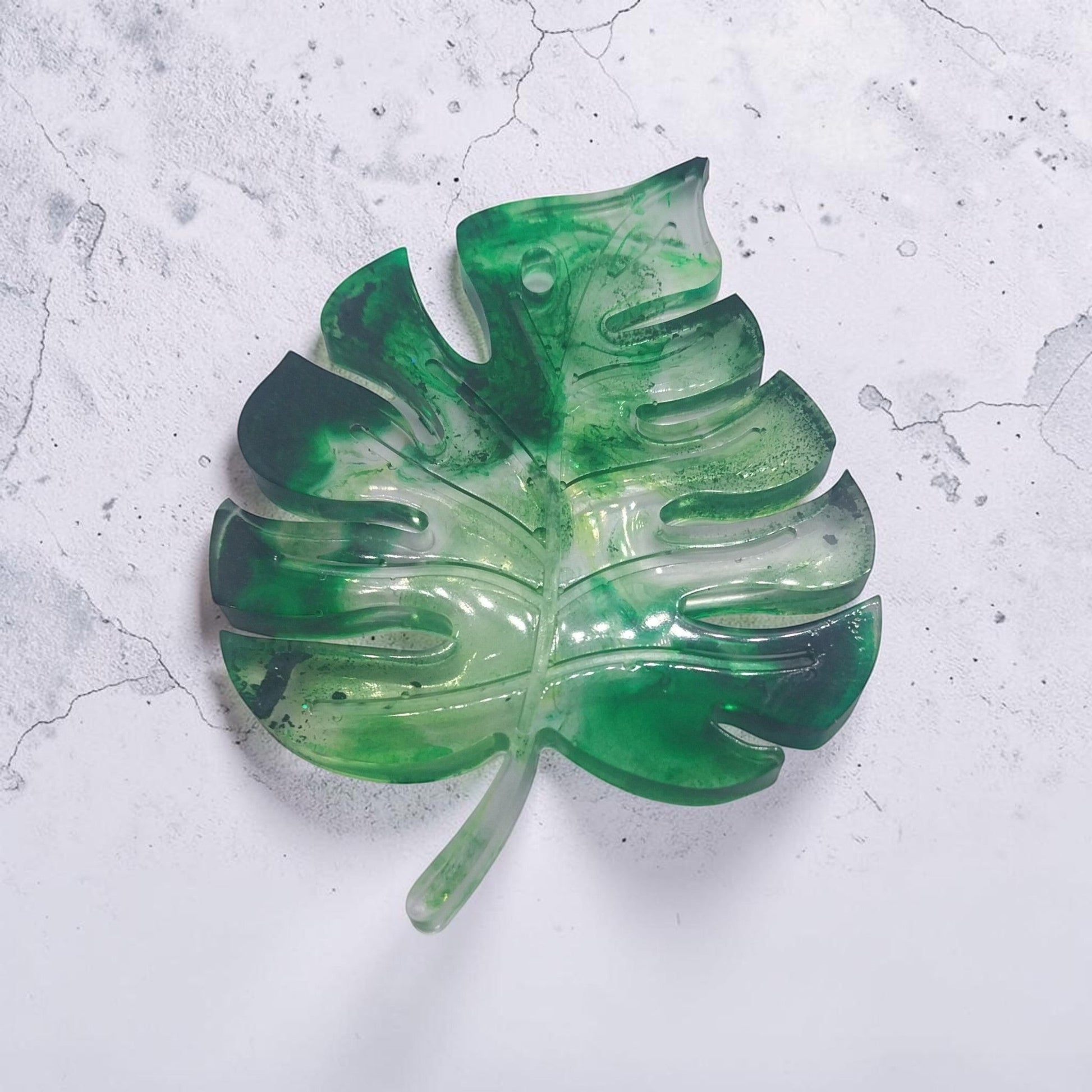 Artymunk3y monstera leaf shaped resin tray in marbled forest green with a glossy finish on a textured white surface.