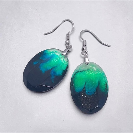 Artymunk3y handcrafted oval resin drop earrings featuring a swirling black, emerald green, and teal nebula pattern.