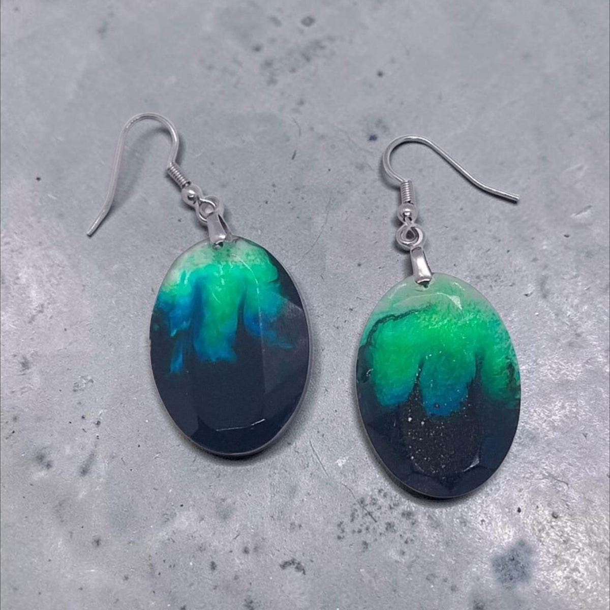 Artymunk3y handcrafted oval resin drop earrings featuring a swirling nebula pattern in black, emerald green, and teal.