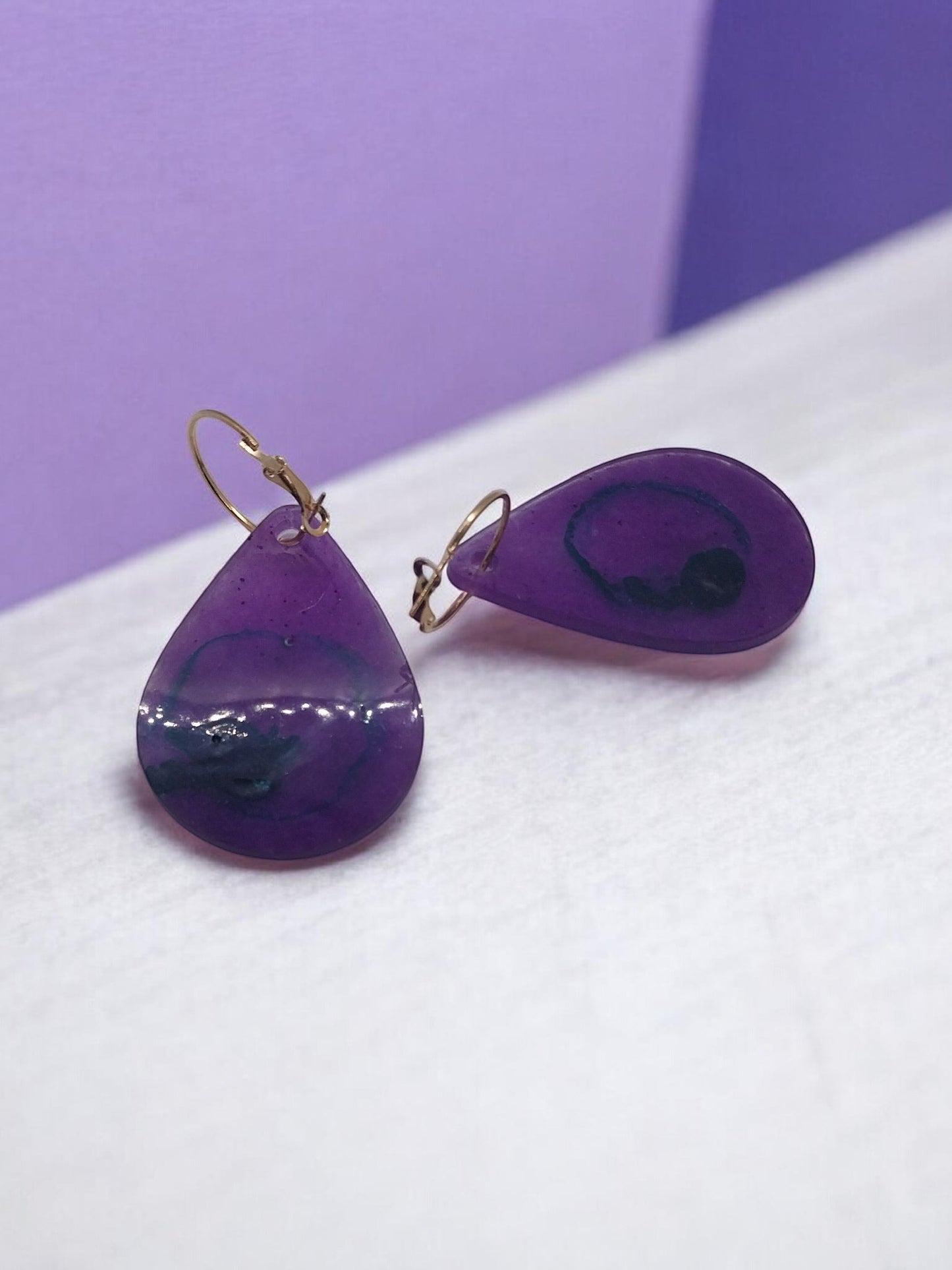 Artymunk3y teardrop resin dangle earrings in translucent purple with blue and black swirls, gold-toned leverback closures.