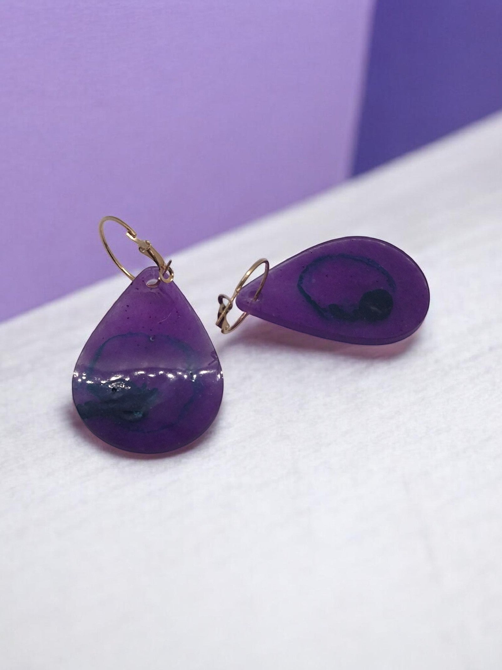 Artymunk3y teardrop resin dangle earrings in translucent purple with blue and black swirls, gold-toned leverback closures.