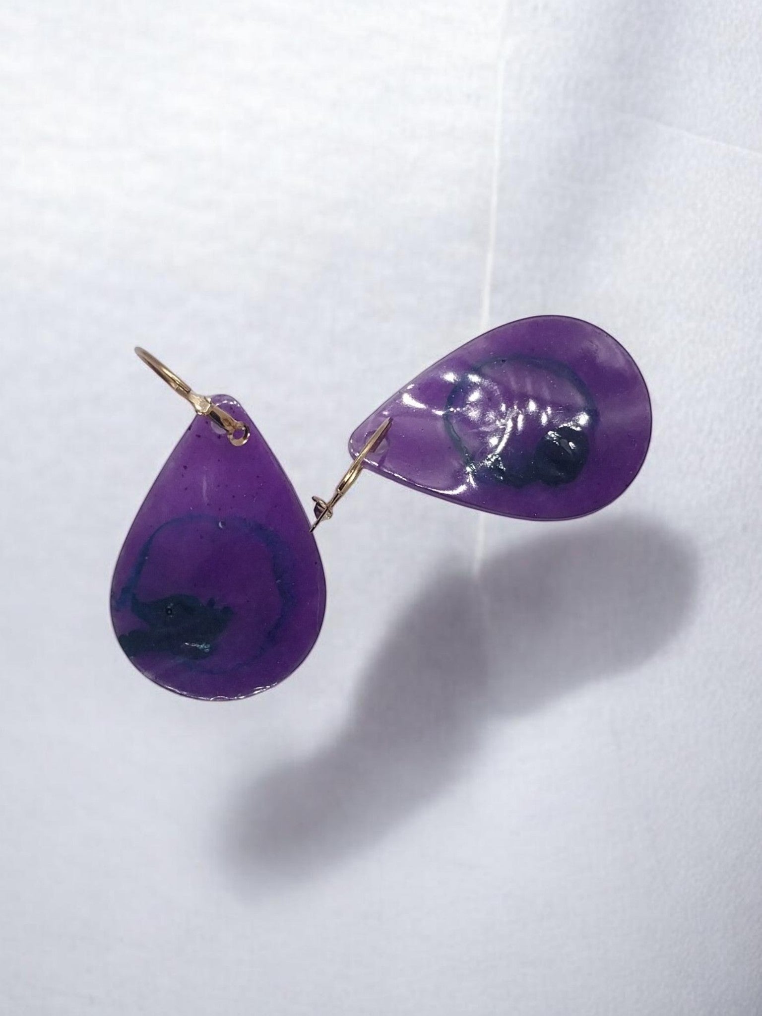Artymunk3y teardrop resin dangle earrings in translucent purple with blue and black swirls, gold leverback closures.