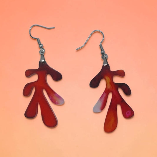 Artymunk3y organic drop earrings in fiery red and orange marbled resin with silver-toned hooks on a peach background.