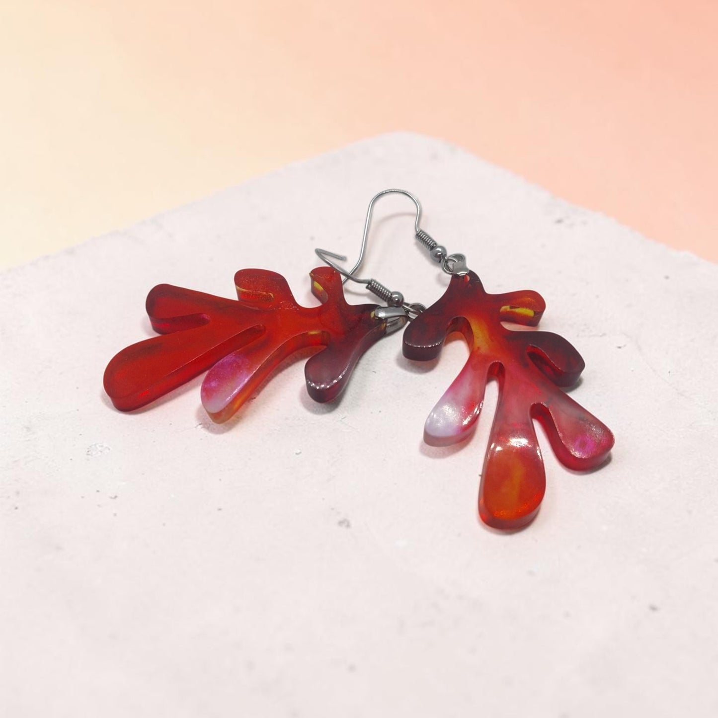 Artymunk3y organic drop earrings in translucent red and orange marbled resin with silver-toned hooks on a stone base.