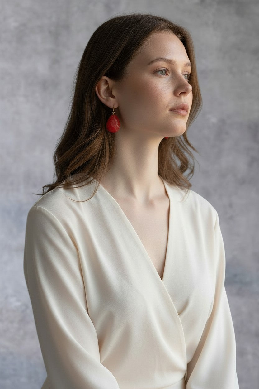 Artymunk3y faceted red teardrop dangle earrings with gold hooks worn by a woman in a cream blouse