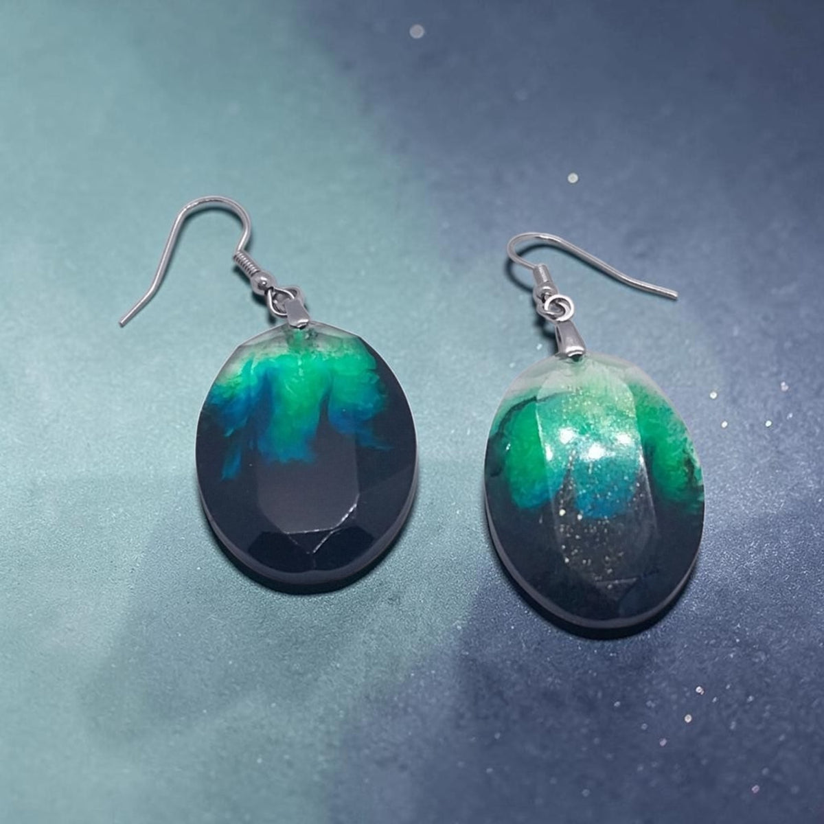 Artymunk3y handcrafted resin oval drop earrings with swirling emerald green, teal, and black nebula patterns.
