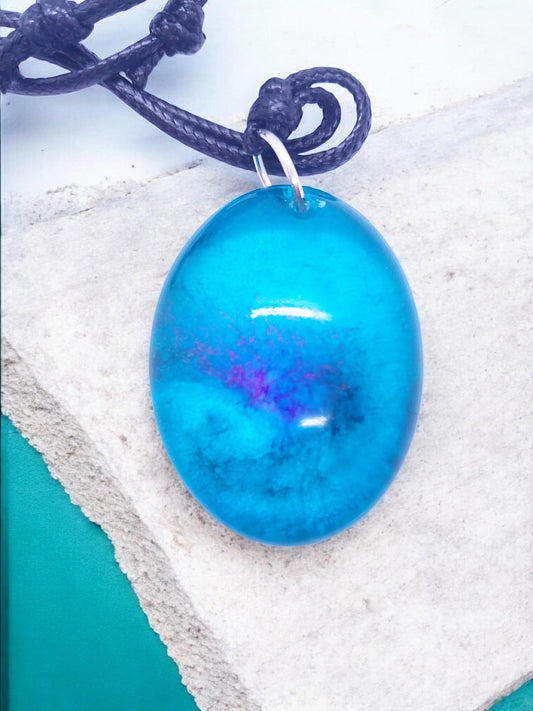 Artymunk3y blue resin oval pendant necklace with black cord, featuring swirls of magenta and indigo.