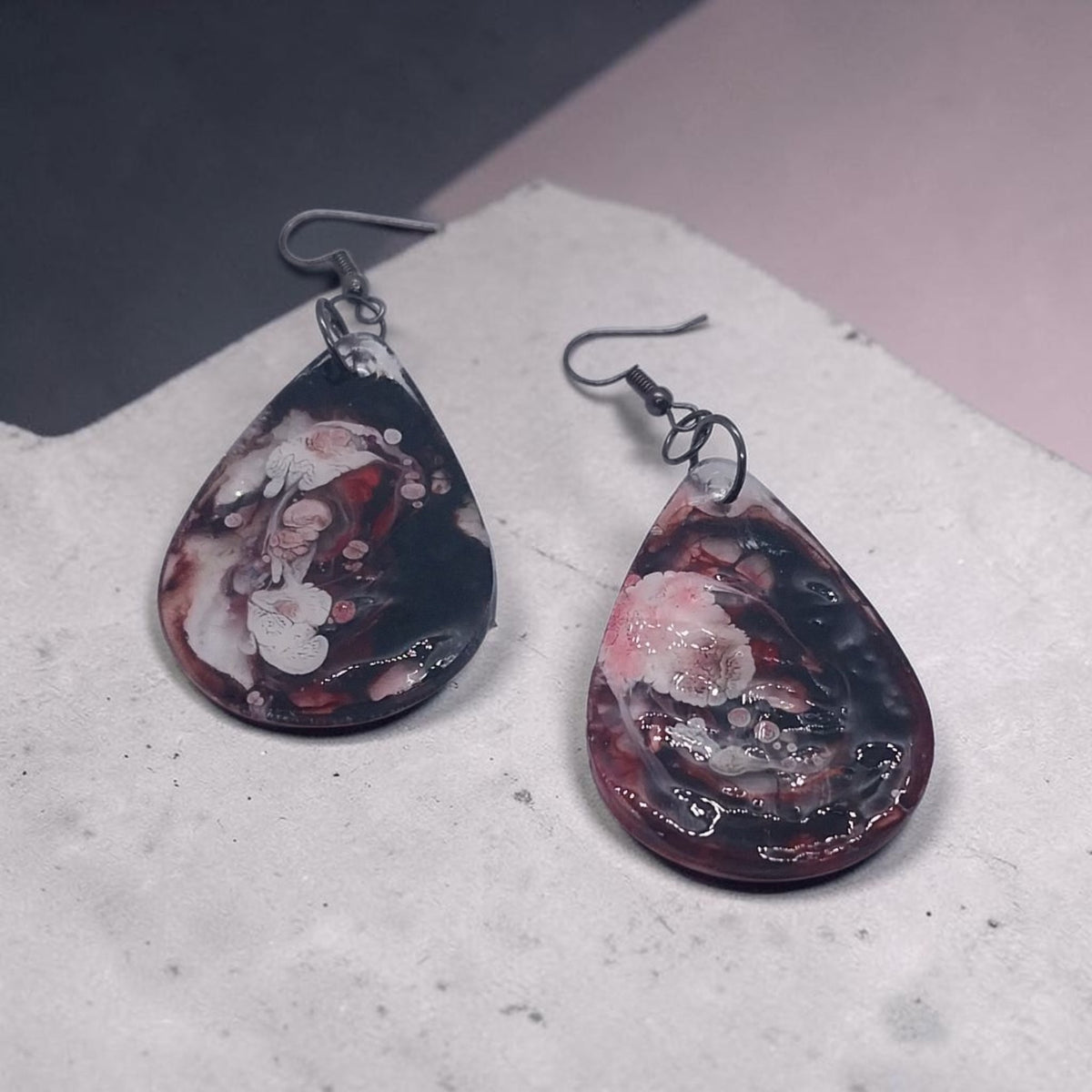 Artymunk3y handcrafted resin teardrop earrings with a black, crimson, and white marble swirl pattern on dark hooks.