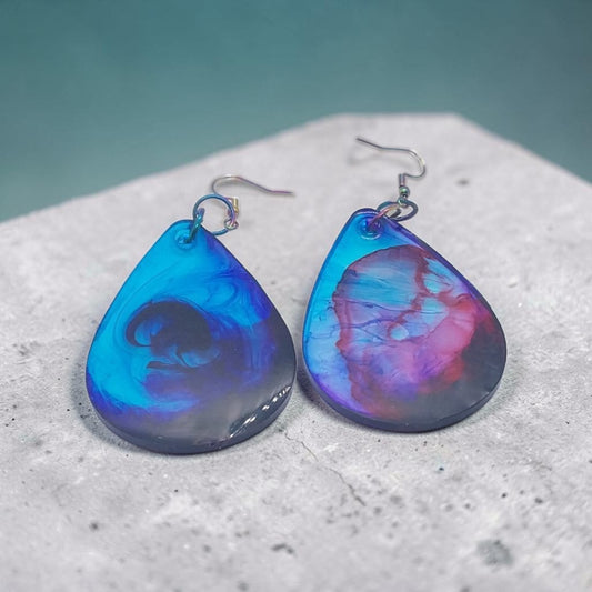Artymunk3y handcrafted resin teardrop earrings with a galaxy-inspired swirl of blue, purple, and pink on a stone base.