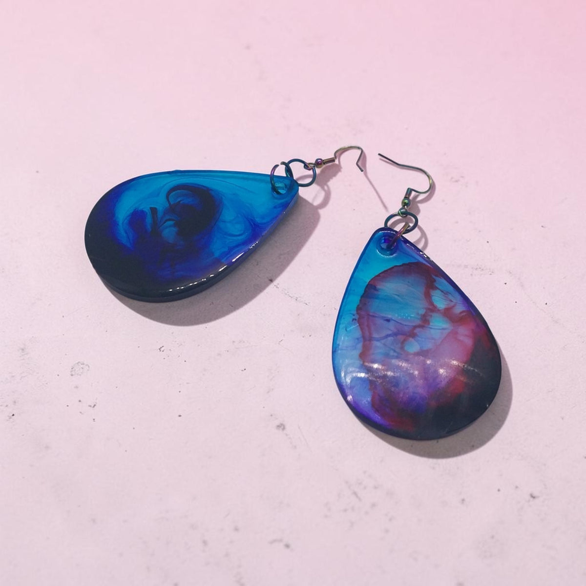 Artymunk3y handcrafted resin teardrop earrings with a swirling galaxy pattern in blue, purple, and pink on hooks.