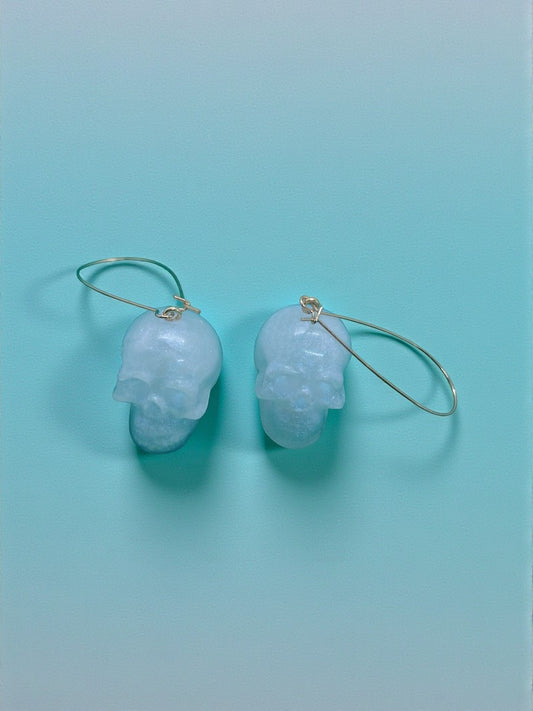 Artymunk3y pale blue translucent skull shaped dangling earrings with gold hoops.