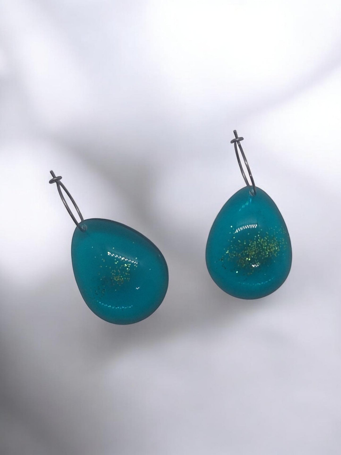 Artymunk3y teal teardrop glitter hoop earrings with silver-tone hoops. Translucent material with gold glitter flecks.