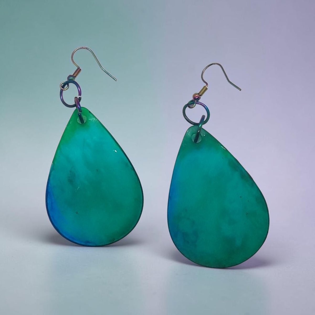 Artymunk3y handcrafted teardrop dangle earrings in a teal and blue gradient with iridescent metal hooks.