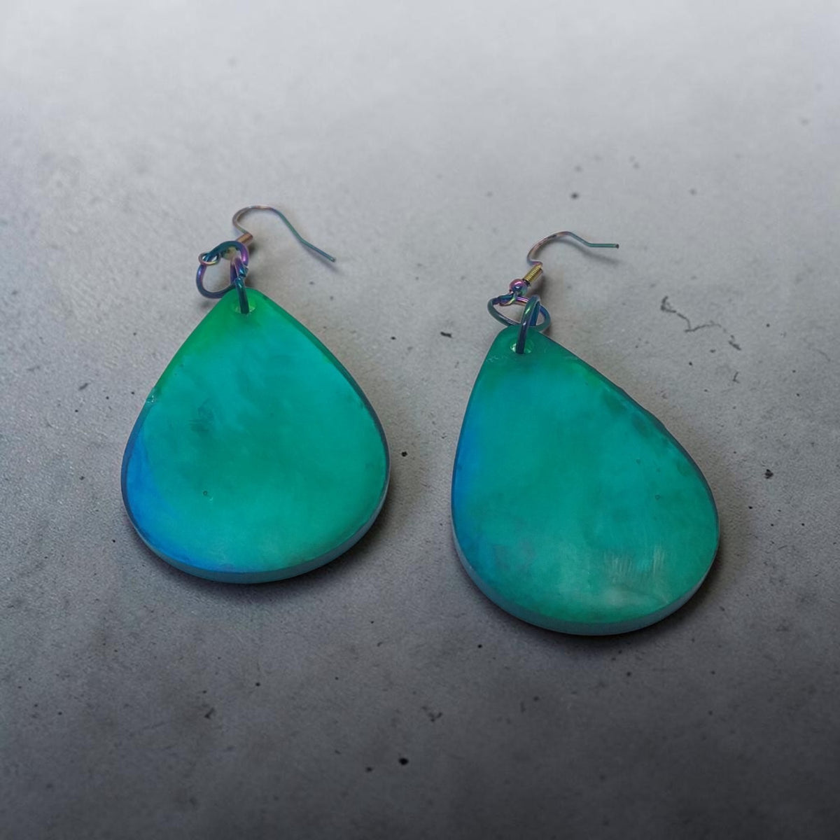 Artymunk3y handcrafted teardrop dangle earrings with a teal and blue gradient finish and iridescent metal hooks.