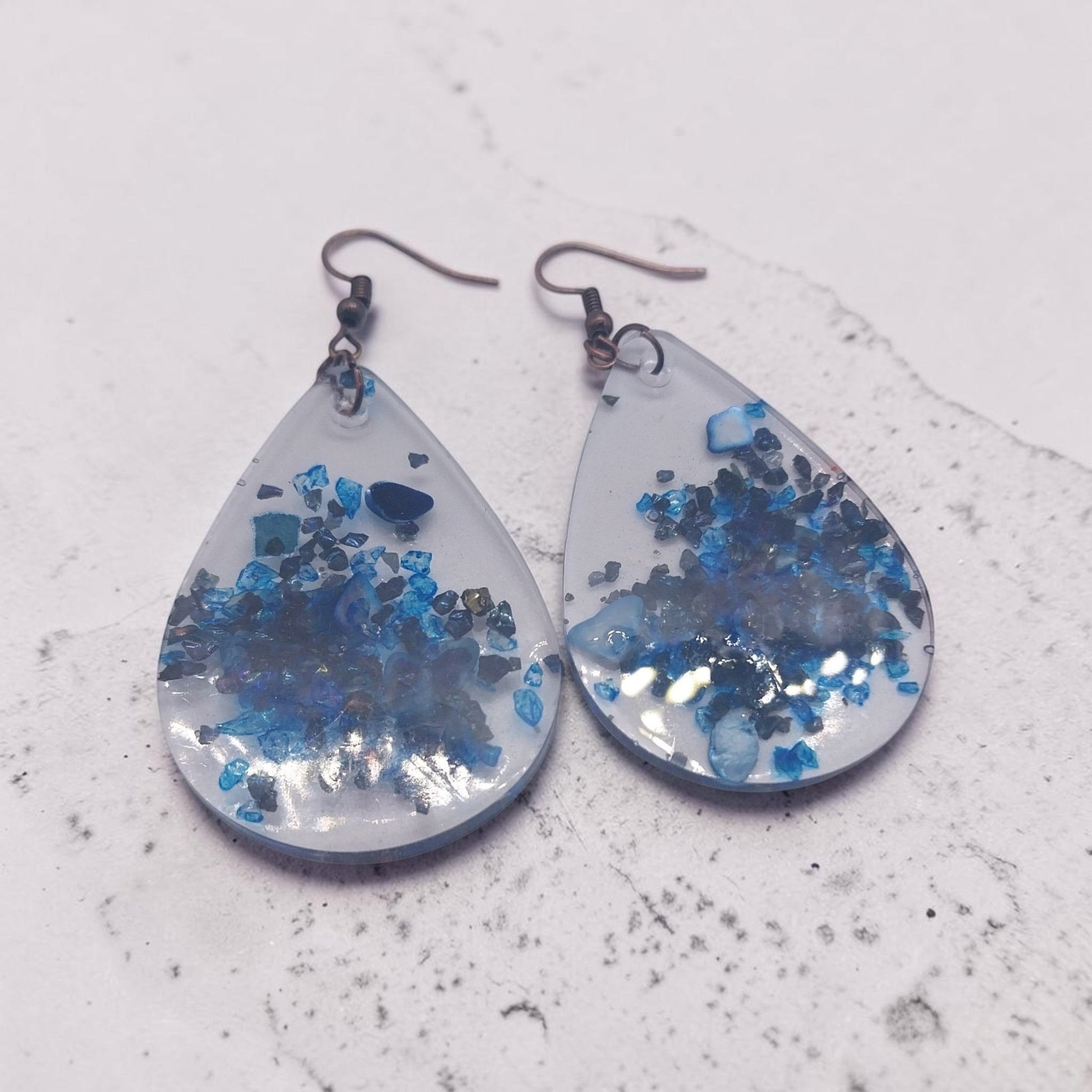 Artymunk3y teardrop dangle earrings featuring clear resin with deep blue crushed stone accents and rustic metal hooks.