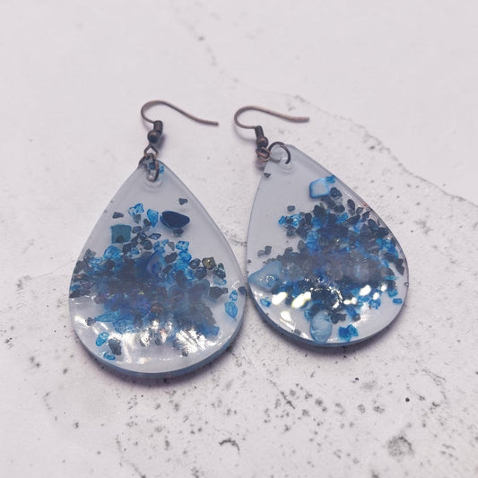 Artymunk3y teardrop dangle earrings featuring clear resin with deep blue crushed stone accents and rustic metal hooks.
