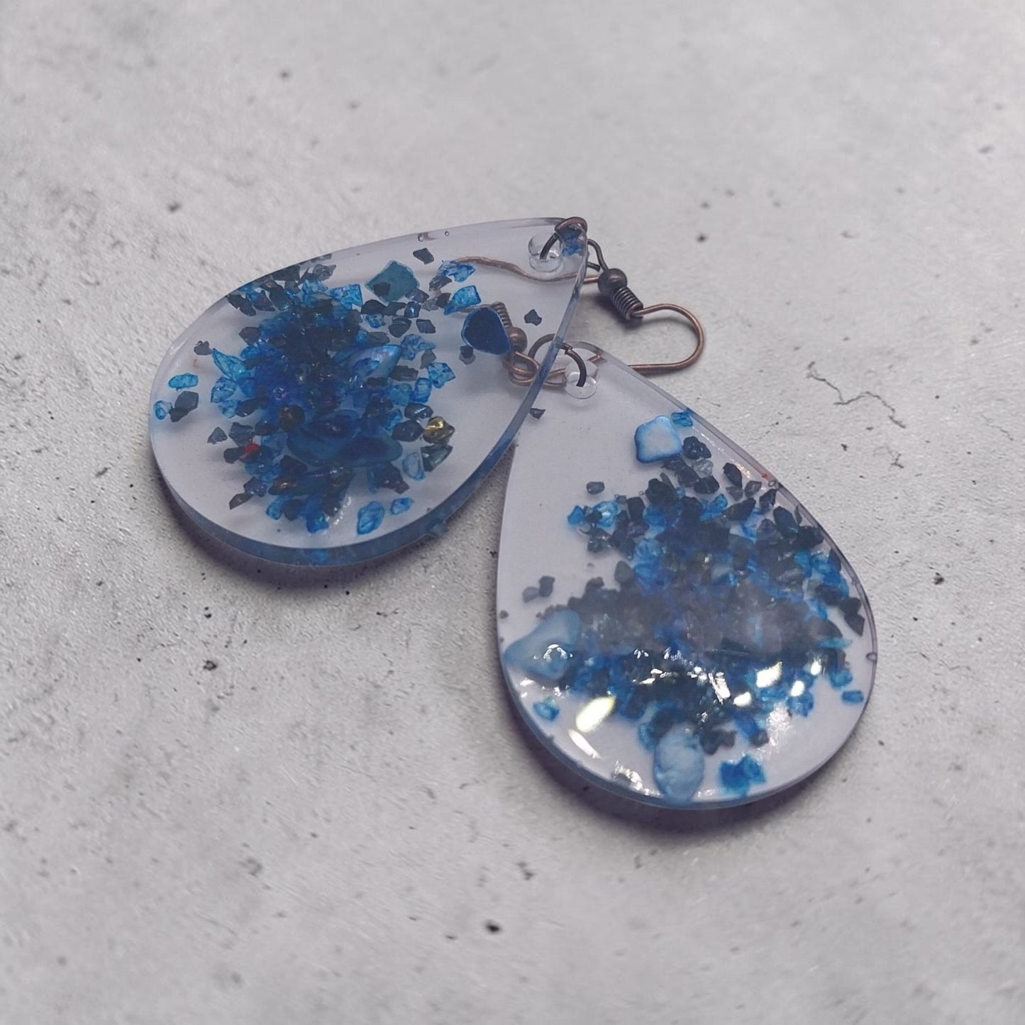 Artymunk3y teardrop resin dangle earrings featuring deep blue crushed stone accents and rustic metal hooks.