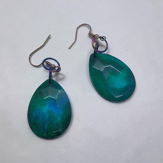 Artymunk3y teardrop dangle earrings in teal and emerald resin with faceted surfaces and iridescent oil-slick hooks.