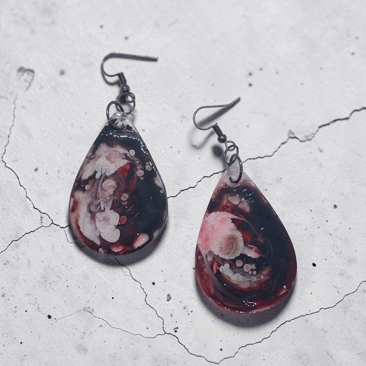 Artymunk3y handcrafted teardrop resin earrings with a black, crimson, and white marble swirl pattern on metal hooks.