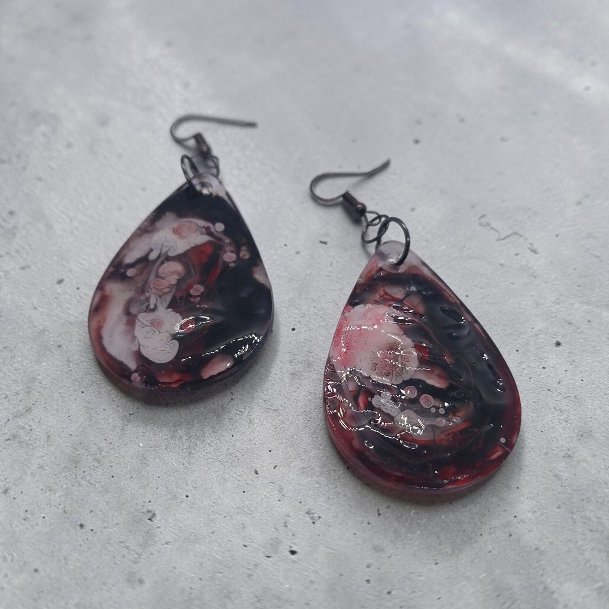 Artymunk3y handcrafted teardrop resin earrings with a black, crimson, and white marble swirl pattern on metal hooks.